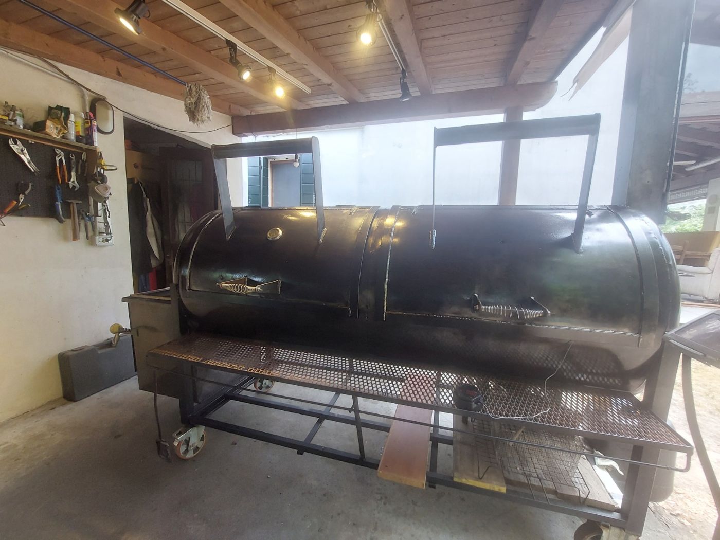 Un grande offset smoker nero a doppia porta sotto un porticato