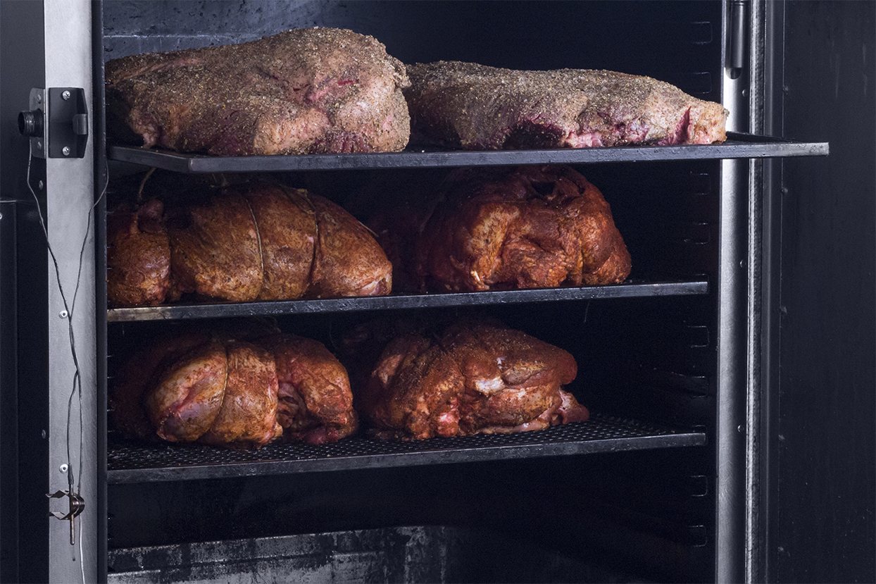 Brisket e spalle di maiale speziate sulle griglie dello smoker, prima della cottura